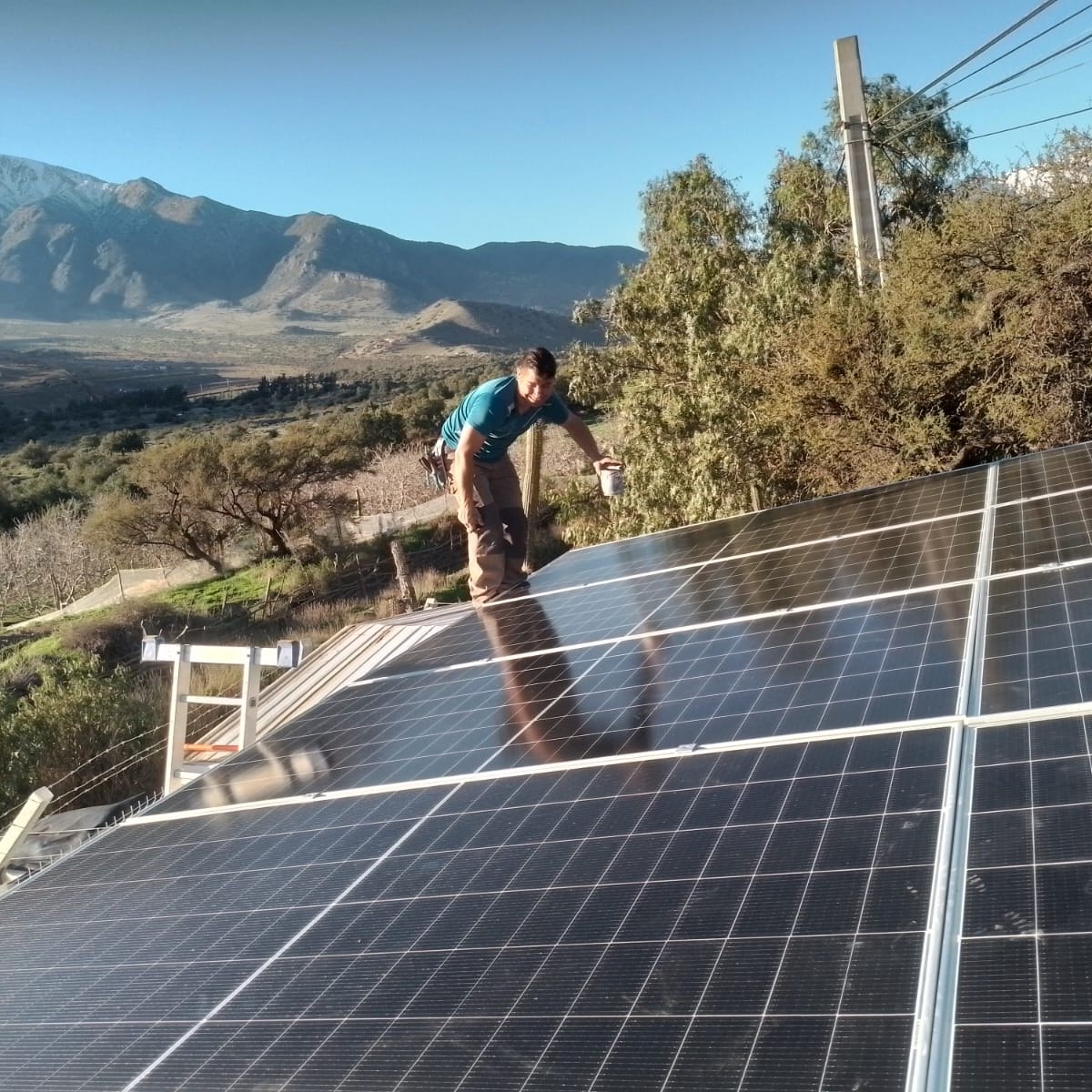 Paneles solares instalados sobre techo para un comité de Agua Potable Rural, con cerros nevados al fondo